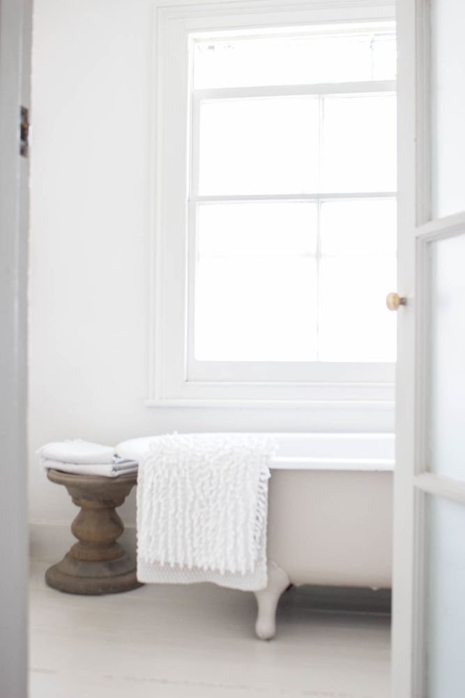 White shabby chic vintage boho bathroom design with clawfoot tub and round wood accent pedestal - Atlanta Bartlett.